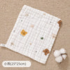 A white quilted muslin baby burp cloth towel with small animal embroidery rests on a beige fabric background.