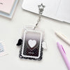 A clear acrylic photocard holder with a heart design and angel wings is displayed on a white surface.