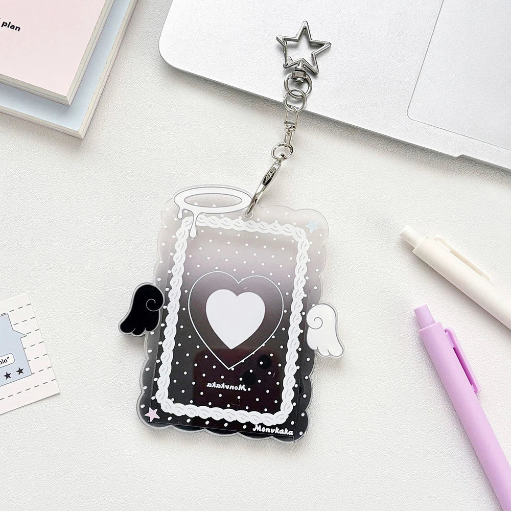 A clear acrylic photocard holder with a heart design and angel wings is displayed on a white surface.
