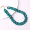 A teal acrylic statement choker necklace with a gold-tone chain is displayed on a white background.