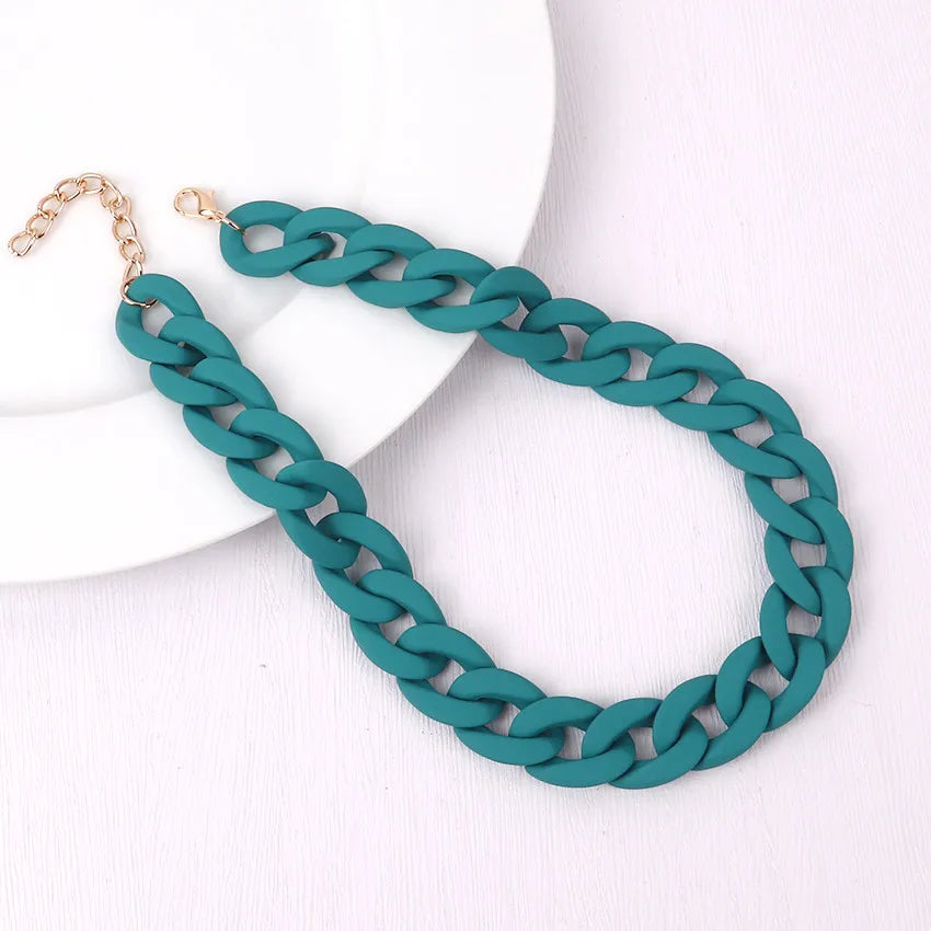 A teal acrylic statement choker necklace with a gold-tone chain is displayed on a white background.