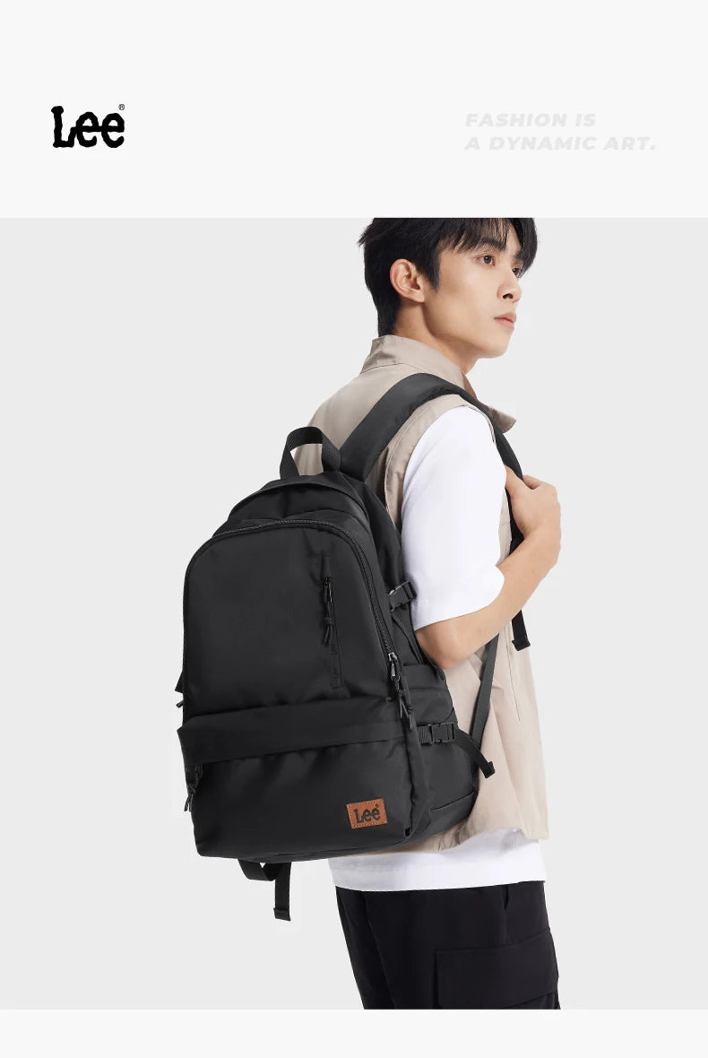 A young man wearing a beige jacket and white shirt carrying a black Oxford school backpack.