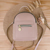 A light pink waterproof PU mini backpack with a zipper closure is displayed on a woven mat next to dried natural elements.