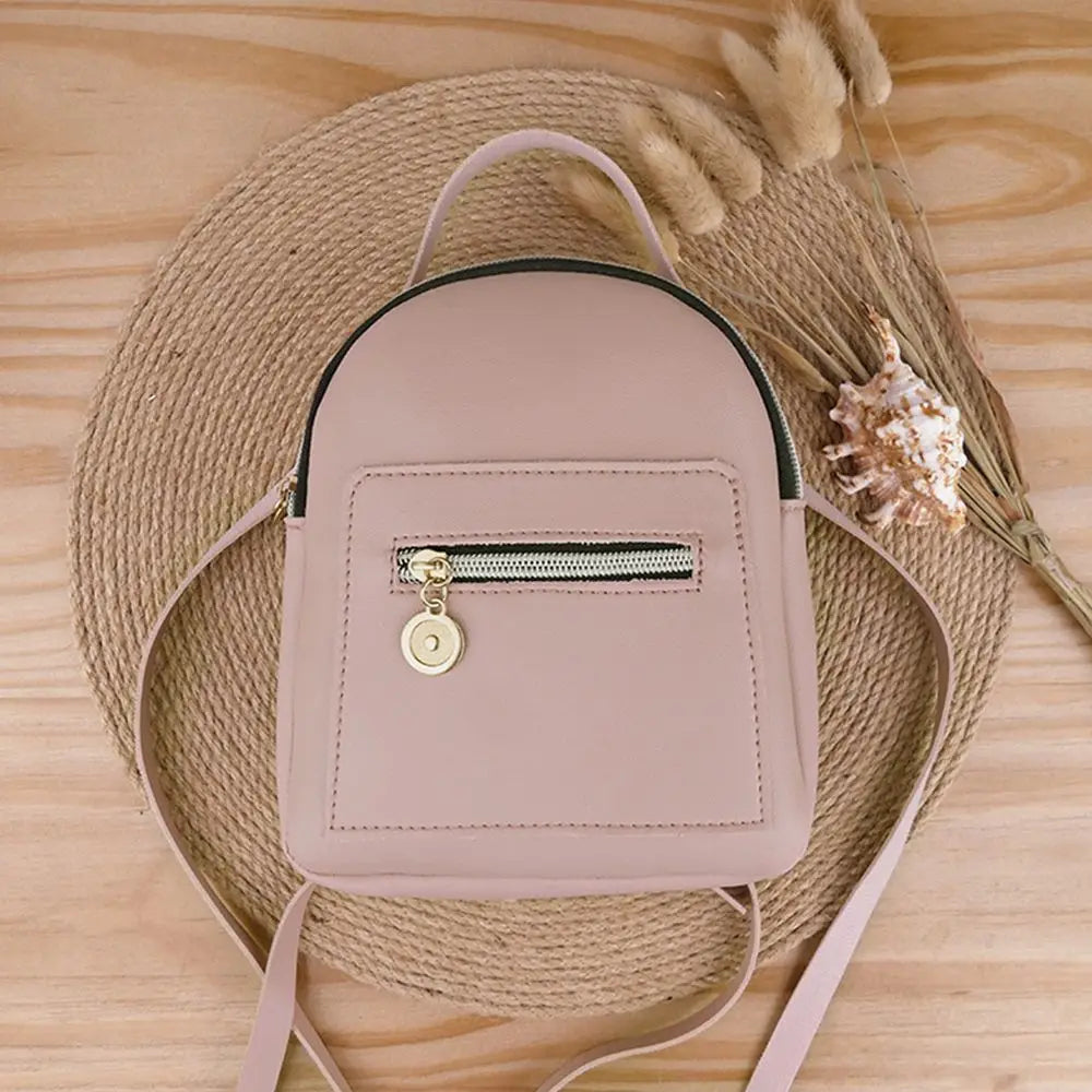 A light pink waterproof PU mini backpack with a zipper closure is displayed on a woven mat next to dried natural elements.