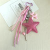 Clé-pendant en forme d'étoile scintillante rose avec un charm à cœur et un cordon rose sur une carte blanche.