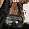 A black PU leather crossbody messenger bag with gold hardware is shown being held by a person wearing a brown jacket.