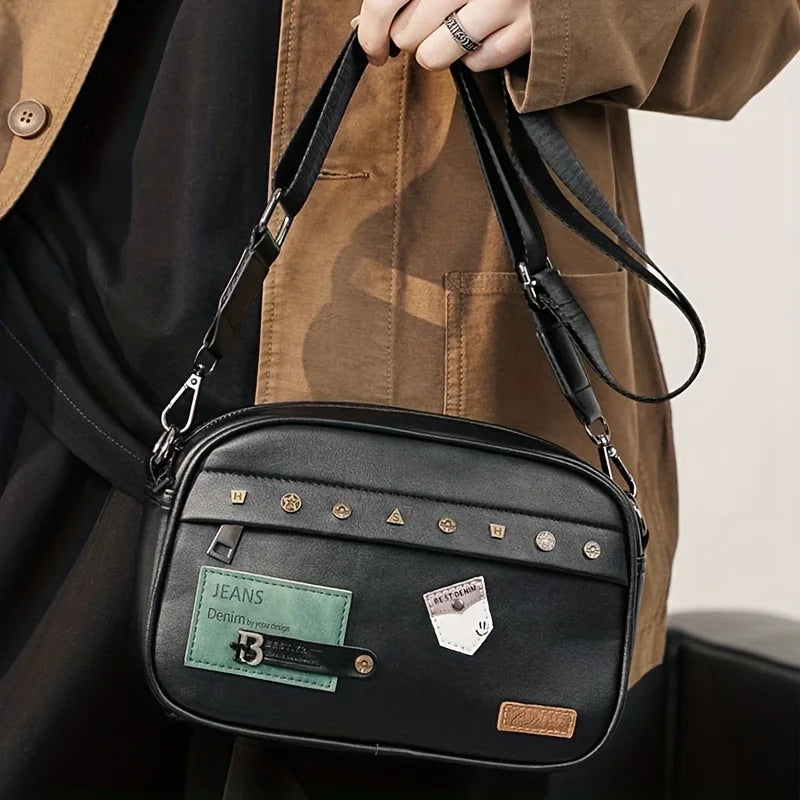 A black PU leather crossbody messenger bag with gold hardware is shown being held by a person wearing a brown jacket.