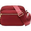 A maroon compact oxford fabric crossbody bag with a strap shown from the front.