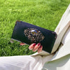 A hand holds a dark green punk style long leather wallet with silver embellishments on bright green grass.