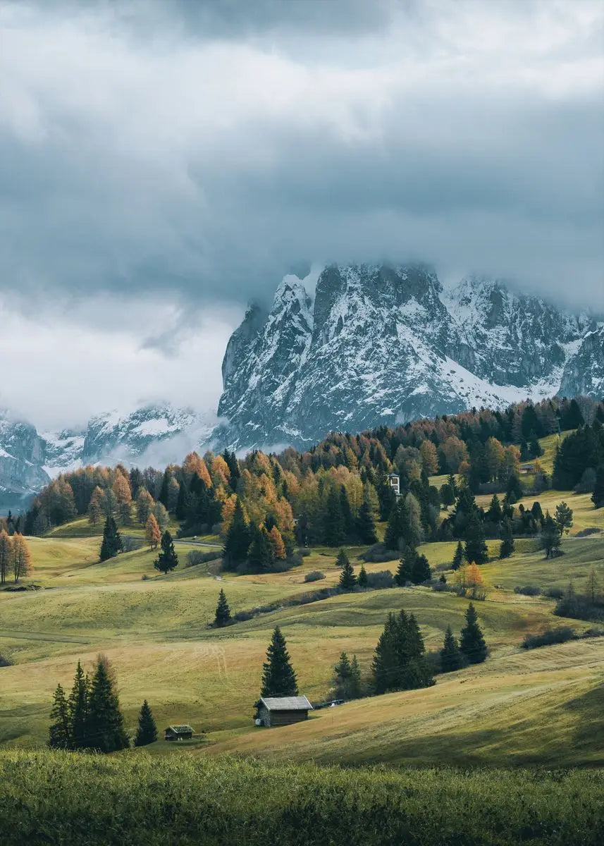 Dramatische Landschaft mit zerklüfteten Bergen, sanften grünen Feldern und dunklen Wolken unter einem stimmungsvollen Himmel.