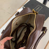 A close-up of a brown vintage PU leather shoulder bag with gold hardware and a zipper, held by a hand.