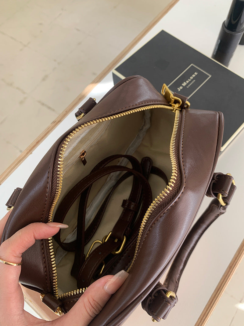 A close-up of a brown vintage PU leather shoulder bag with gold hardware and a zipper, held by a hand.