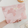 A pink cosmetic organizer bag featuring a pattern of embossed pink bows is held in a person's hand on a white surface.