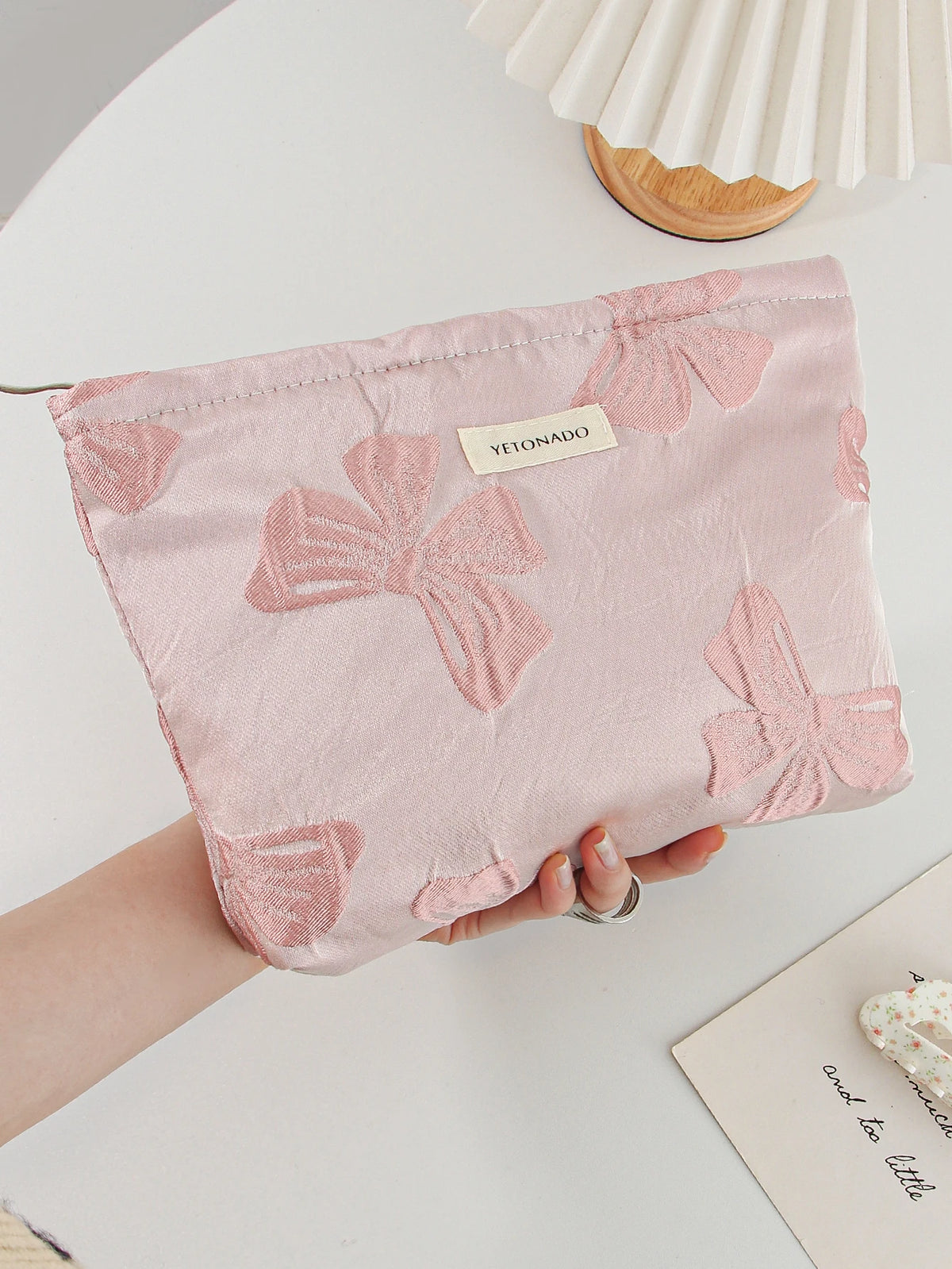 A pink cosmetic organizer bag featuring a pattern of embossed pink bows is held in a person's hand on a white surface.