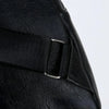 Gros plan d'un sac bandoulière en cuir noir avec une sangle en nylon noir et des éléments métalliques argentés.
