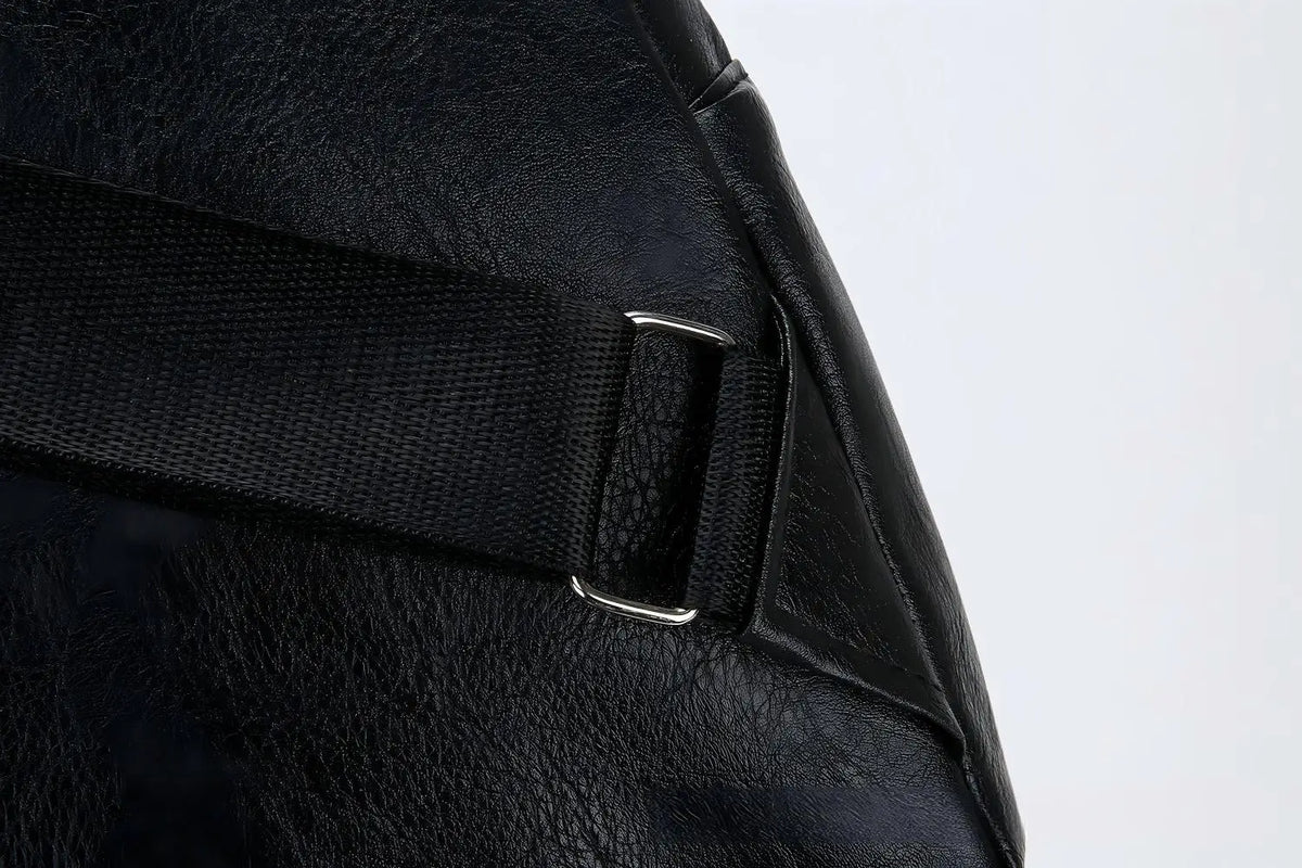 Gros plan d'un sac bandoulière en cuir noir avec une sangle en nylon noir et des éléments métalliques argentés.