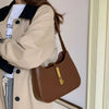 A woman wearing a beige coat holds a brown PU leather hobo shoulder bag.