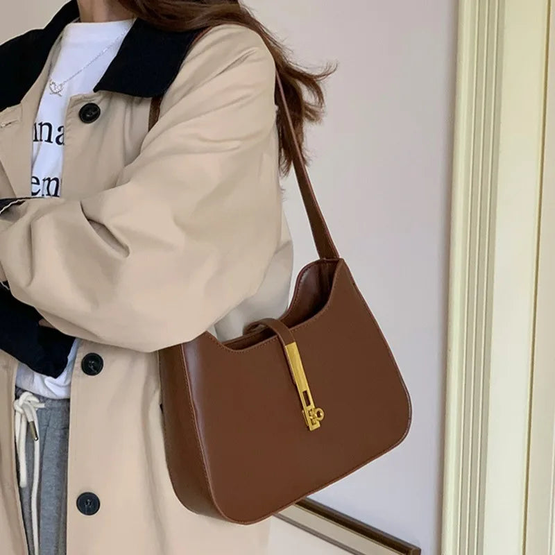 A woman wearing a beige coat holds a brown PU leather hobo shoulder bag.