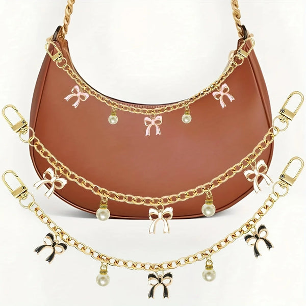 Bolso de cuero marrón con detalles de cadena dorada y adornos de lazo rosa.