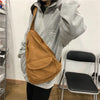 A person is wearing a tan canvas crossbody shoulder bag while sitting in front of a white chair.