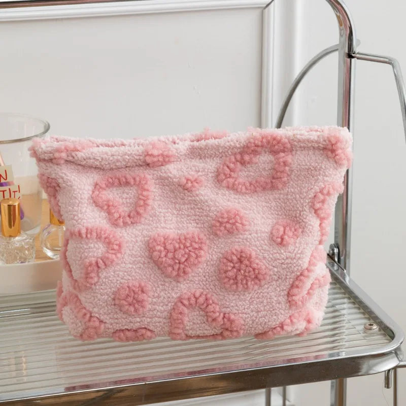 A pink plush storage bag with a heart pattern is displayed on a silver metal shelf.