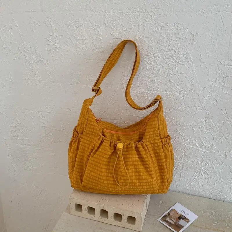 A mustard yellow plaid nylon drawstring tote bag resting on a light surface.