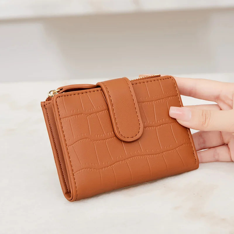 A brown PU leather bifold wallet with a zipper closure is held in a hand on a light surface.