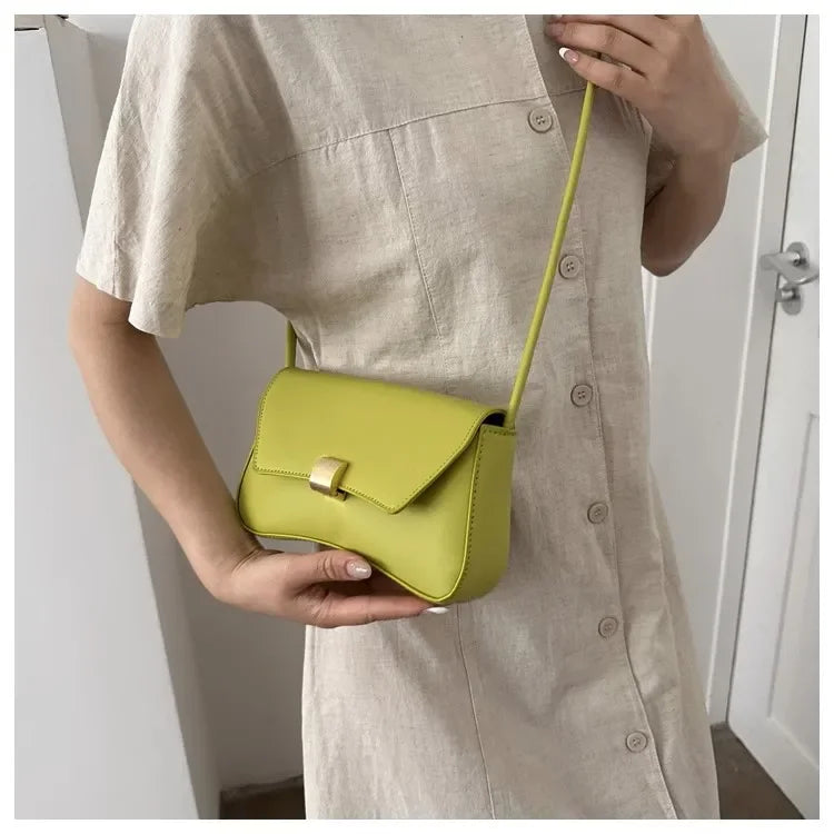 A woman holds a lime green leather crossbody bag against a beige dress.
