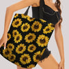 A woman holds a black sunflower canvas tote bag with yellow sunflowers against her torso.