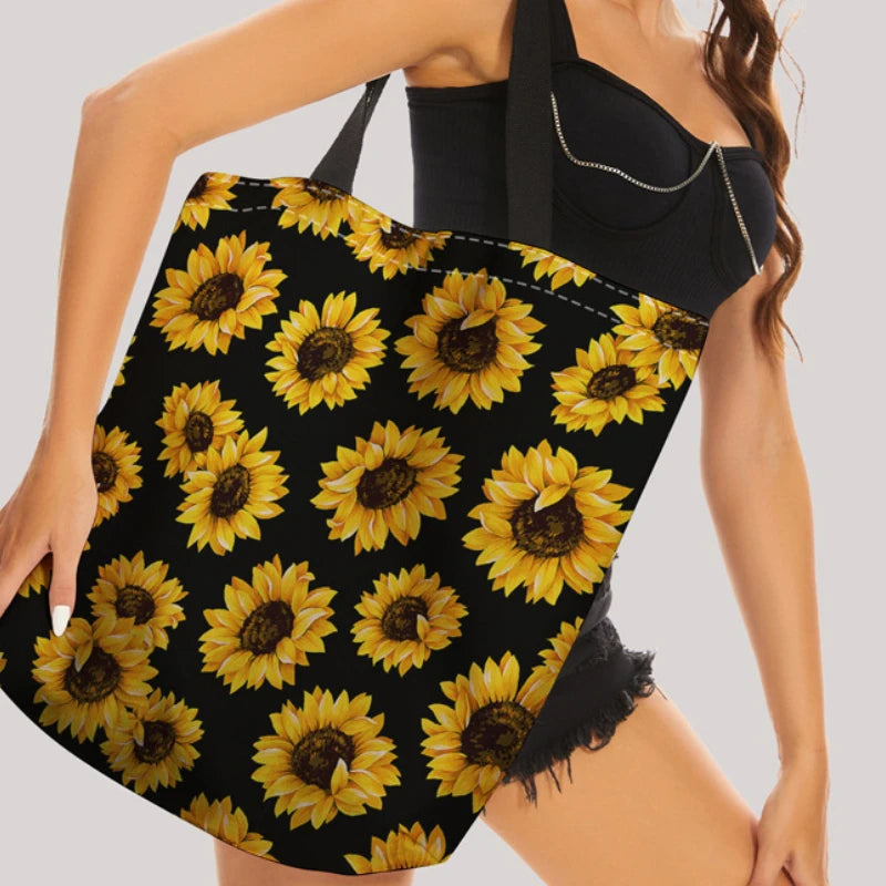 A woman holds a black sunflower canvas tote bag with yellow sunflowers against her torso.