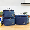 A navy blue insulated lunch tote bag with a black adjustable shoulder strap resting on a wooden surface.