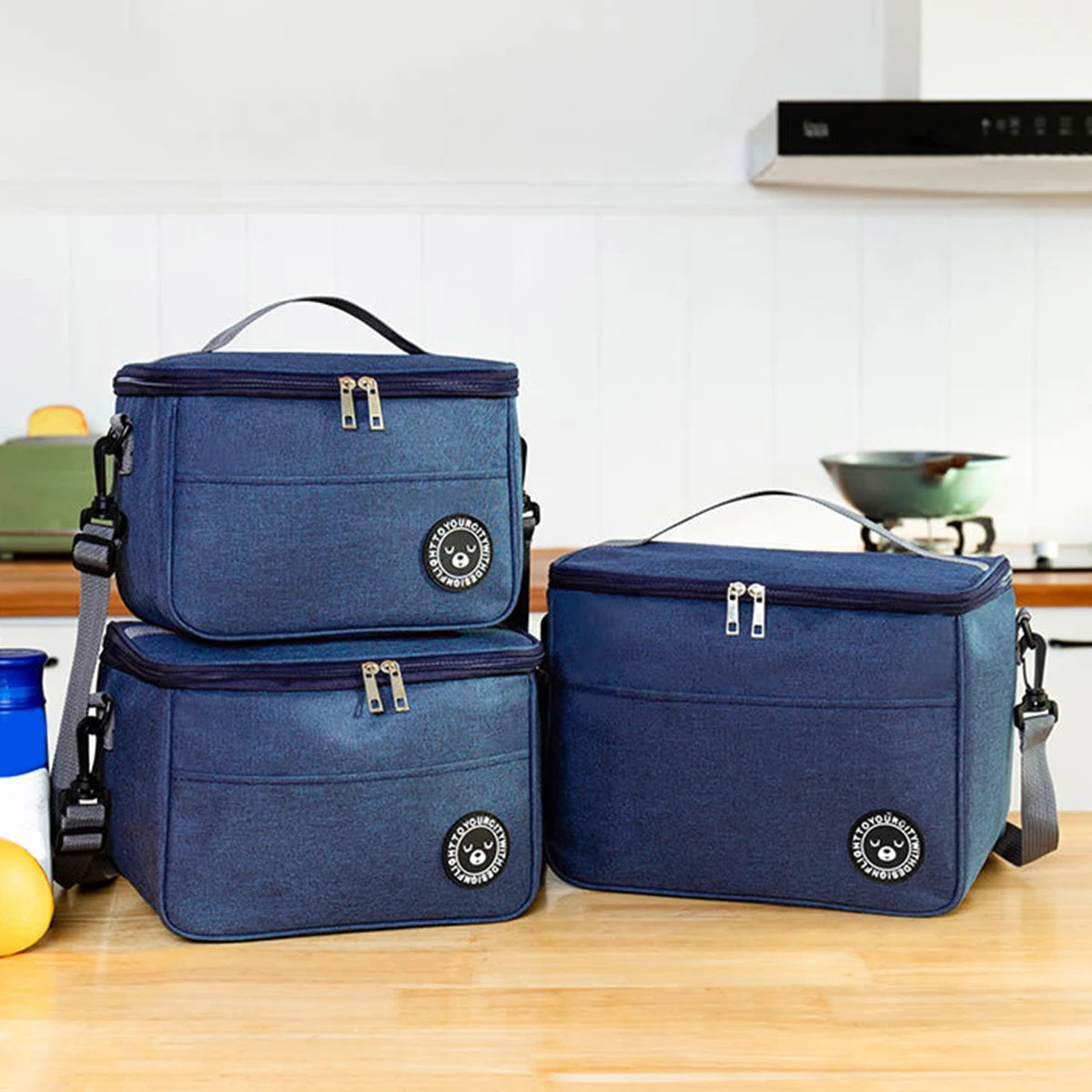 A navy blue insulated lunch tote bag with a black adjustable shoulder strap resting on a wooden surface.