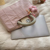 A pink quilted laptop sleeve with a strap and a silver laptop is displayed on a cream textured fabric.
