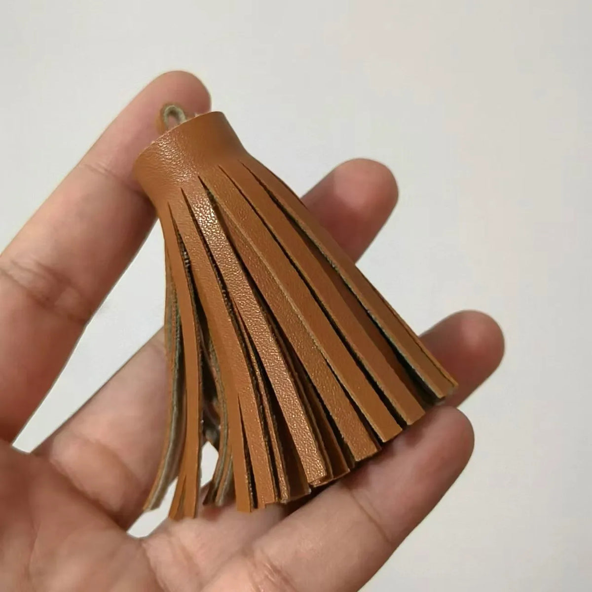 A hand holds a set of brown leather tassel fringe craft supplies.
