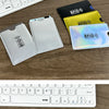 Various colored and clear RFID blocking card sleeves displayed on a wooden surface next to a keyboard.