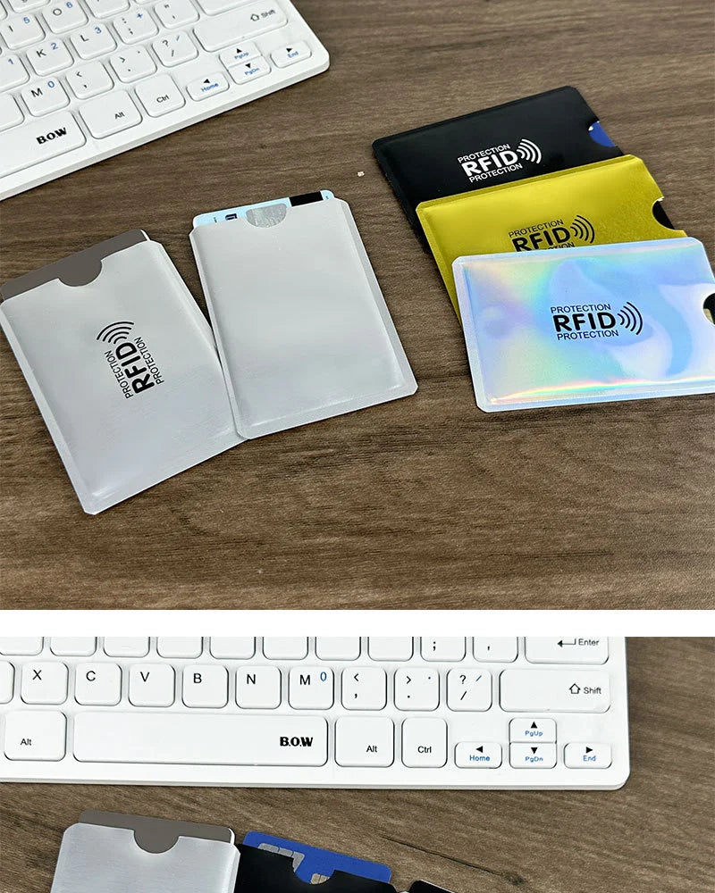 Various colored and clear RFID blocking card sleeves displayed on a wooden surface next to a keyboard.