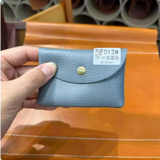 A hand holds a gray leather card holder with a gold stud, displayed on an orange surface.