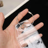 A hand holds a clear luggage tag with a steel ring and a leather cord loop.