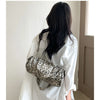 A woman is shown from the back holding a leopard print Rivet Boston shoulder bag against a light background.