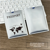Silver RFID metallic passport holder with a world map design placed on a wooden desk next to a laptop keyboard