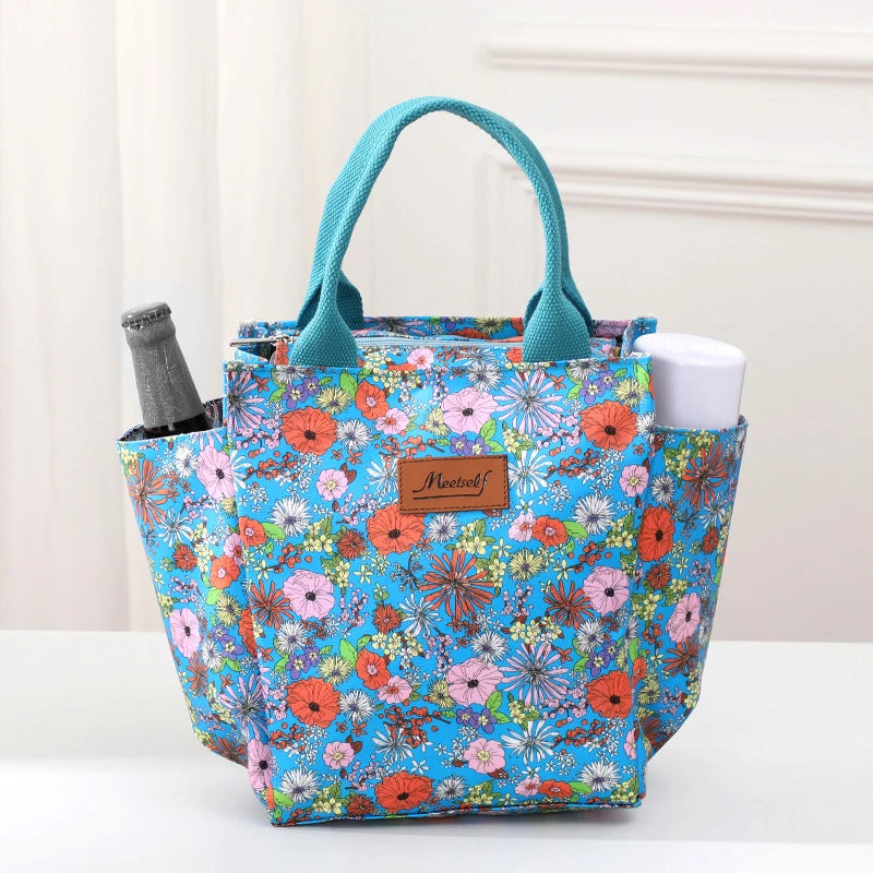 Una bolsa térmica con patrón verde azulado y asa mostrada sobre una superficie blanca.