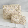 A beige floral print quilted cosmetic bag set resting on a white surface.
