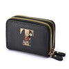 Black faux leather mini wallet with a gold letter T and floral embroidery, featuring a double zipper.