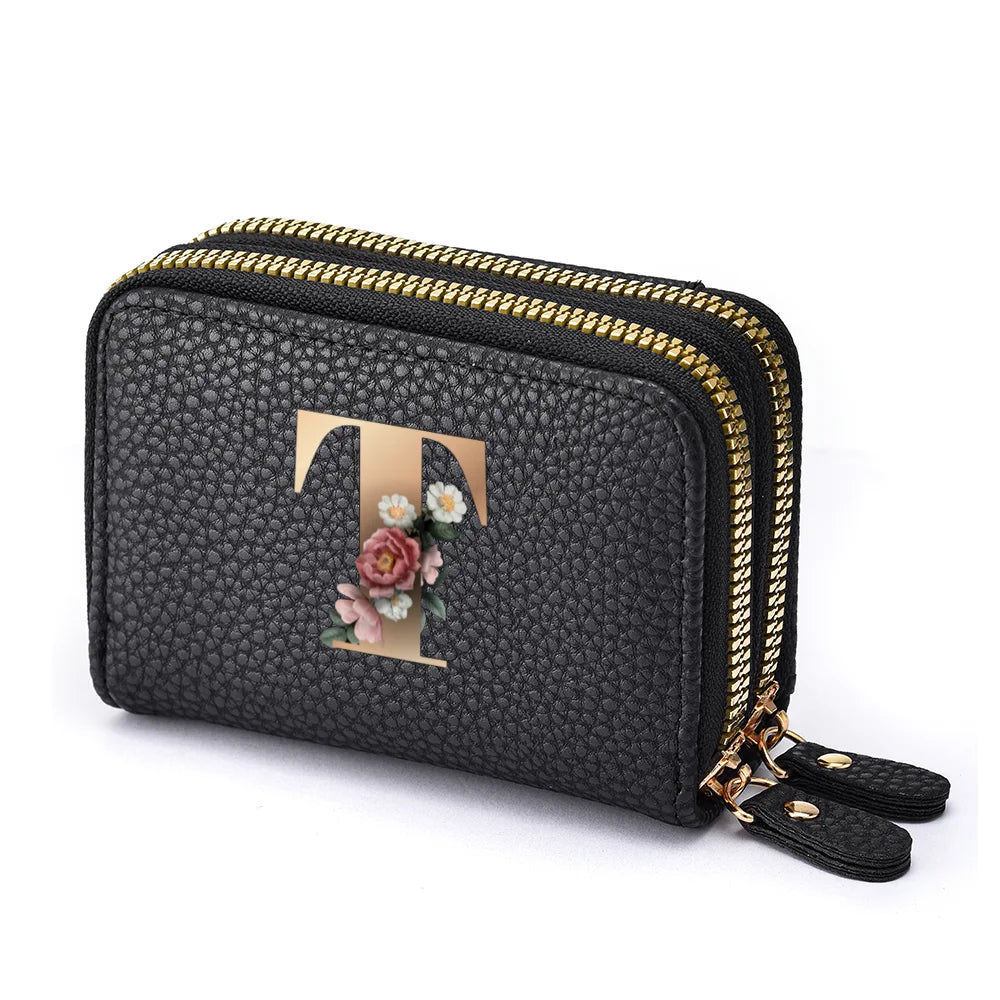 Black faux leather mini wallet with a gold letter T and floral embroidery, featuring a double zipper.