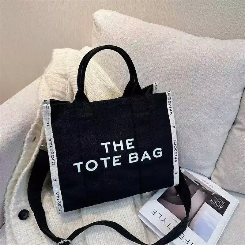 A black tote bag with white text is displayed on a white knitted fabric against a light gray background.