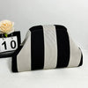 Un sac clutch de plage crochet fait main avec des rayures verticales noir et blanc, posé sur une surface blanche.