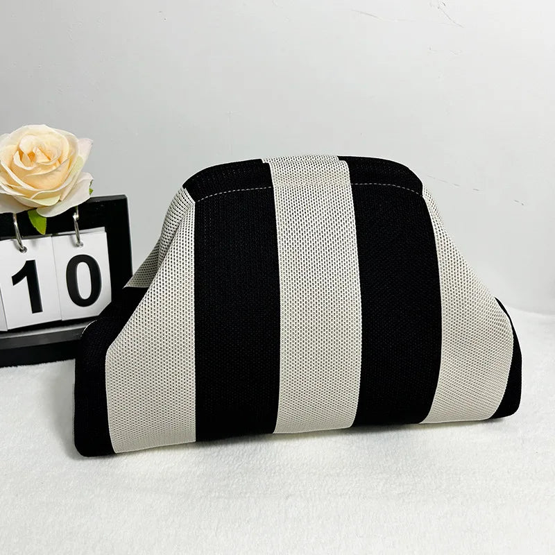 Un sac clutch de plage crochet fait main avec des rayures verticales noir et blanc, posé sur une surface blanche.