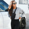 A woman wearing sunglasses and a gray sweater stands next to a white car with a black crossbody storage bag.