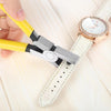 A hand is using a silver leather hole punch plier to create holes in a white leather strap watch band.
