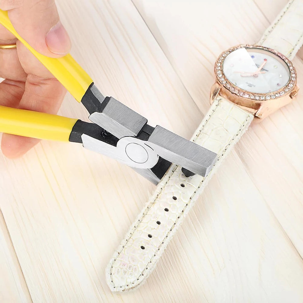 A hand is using a silver leather hole punch plier to create holes in a white leather strap watch band.